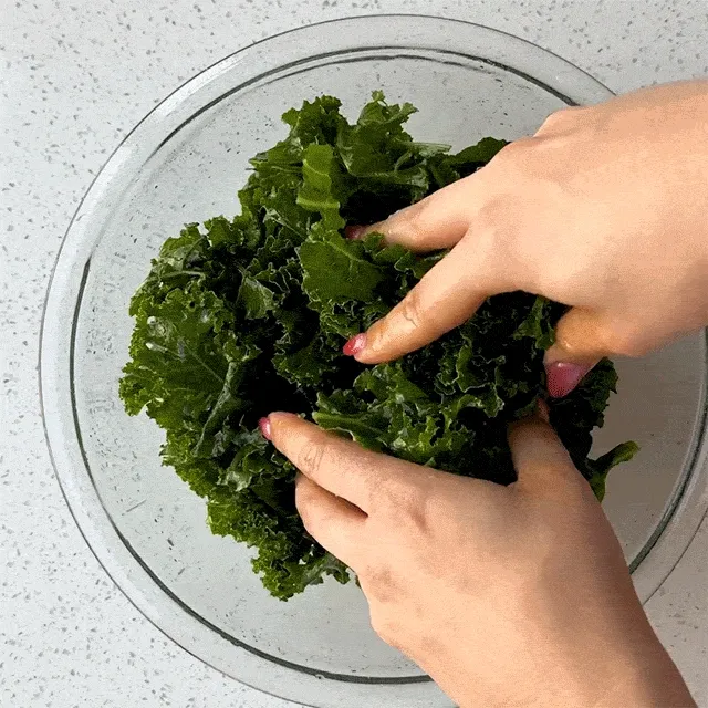 A pair of hands massages kale in a bowl