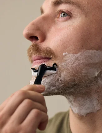 man shaving his beard with black twig razor