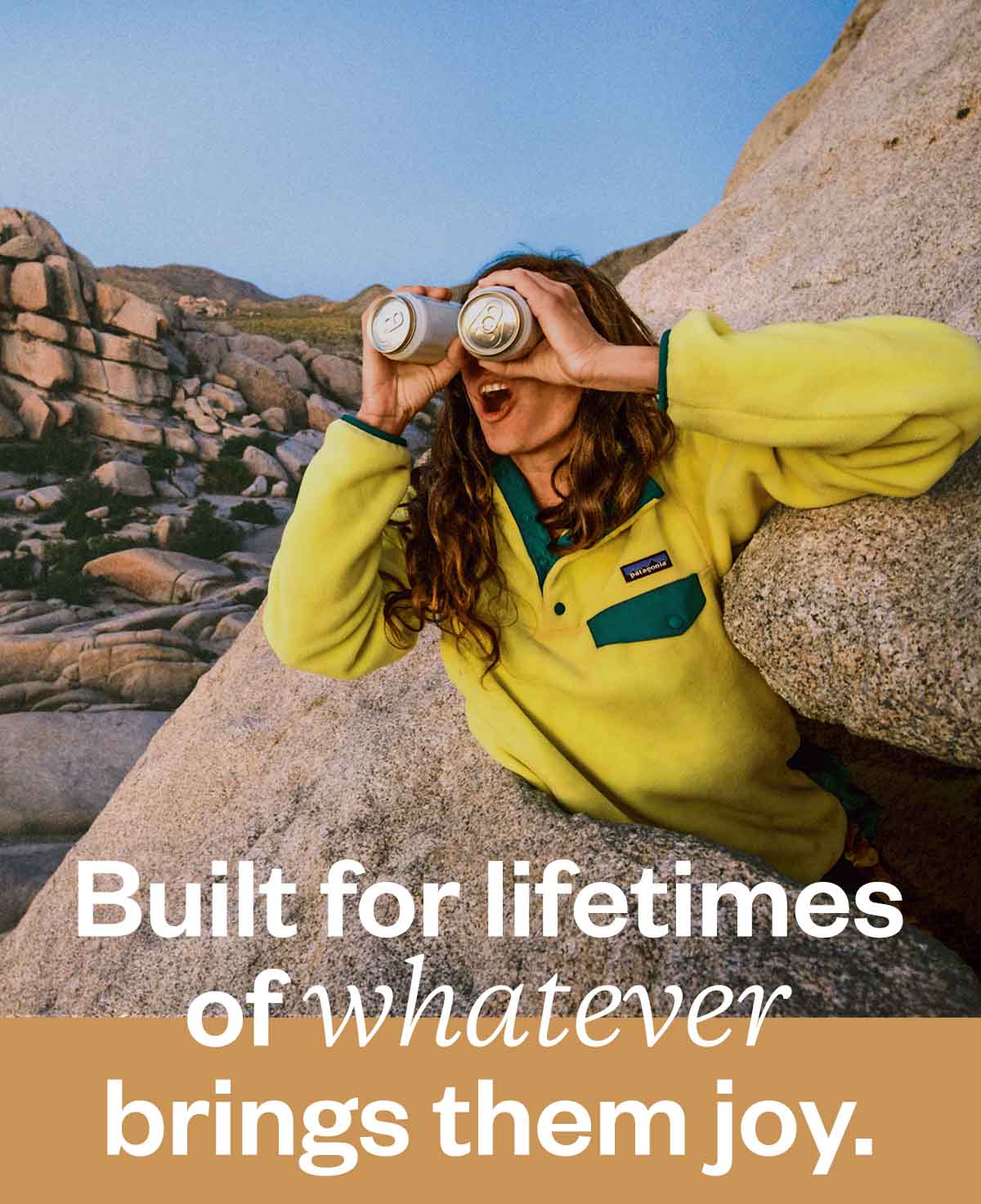 A person holding two beer cans up like binoculars looking out at the rocks in Joshua Tree.