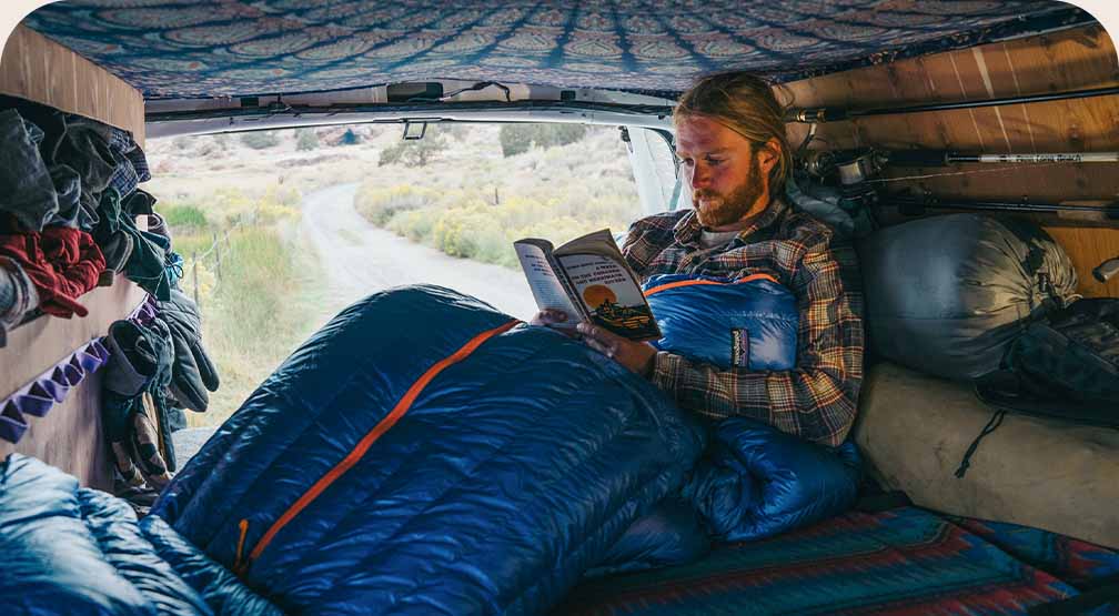 A person reading a book in the bed of a converted truck.