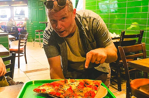 Image Description: A person pointing to pizza on a tray.