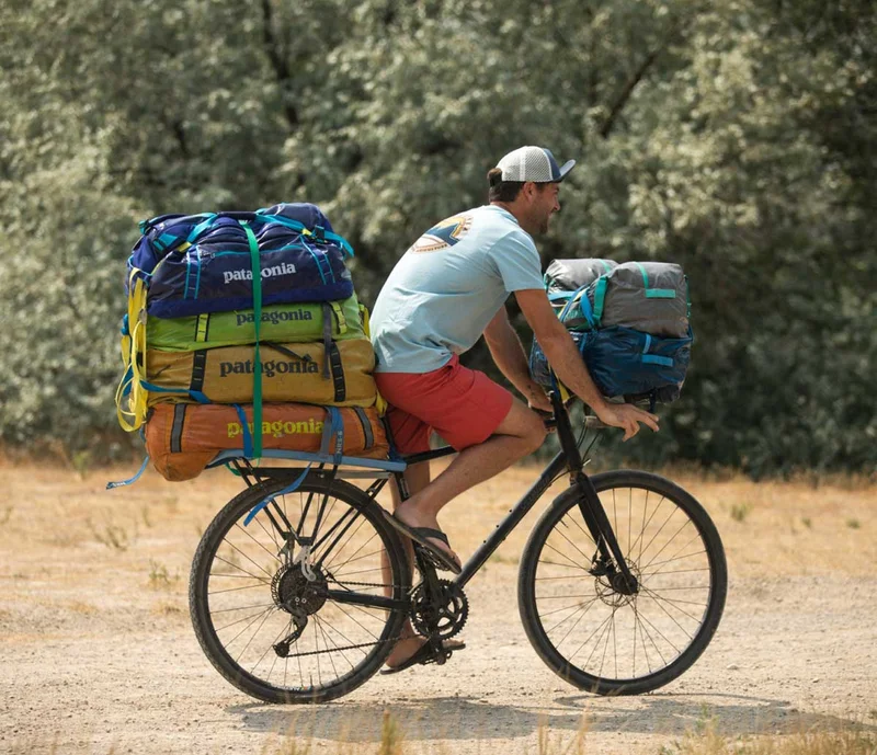 A person on a bike with lots of duffel bags strapped to it.