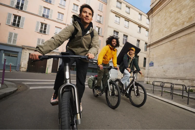 Three friends riding Cowboy bikes through a vibrant city street, enjoying a casual and dynamic ride.