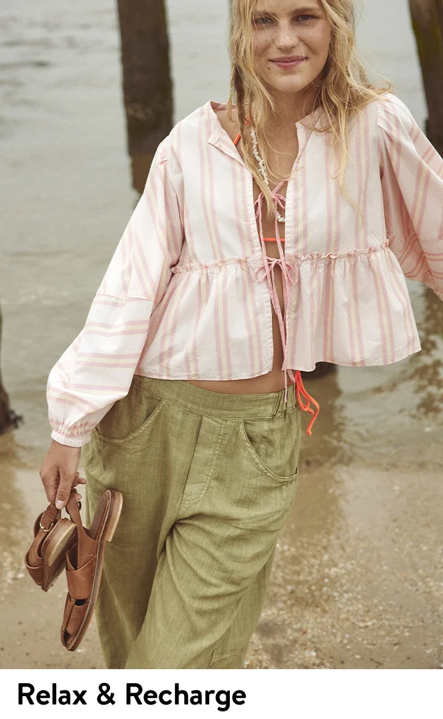 A woman wearing a striped tie-front blouse with green pants.