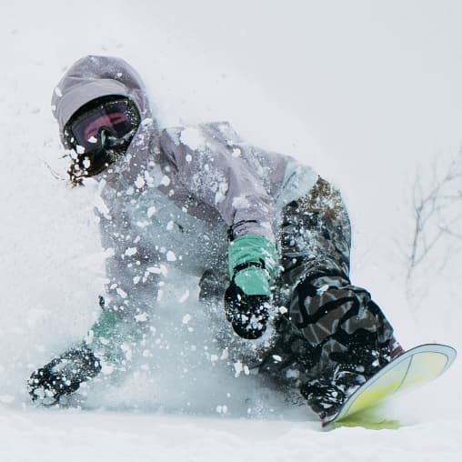 Female snowboarder riding through powder wearing Burton Mittens in teal and wearing Burton Reserve Outerwear.