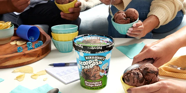 Friends eating ice cream from bowls around a container of Scoop-apalooza Chocolate & Fudge Swirl ice cream.