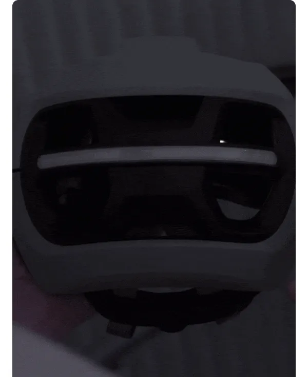 Close-up of a UNIT 1 smart helmet in low light, showing the rear light strip and ventilation details in a dark setting
