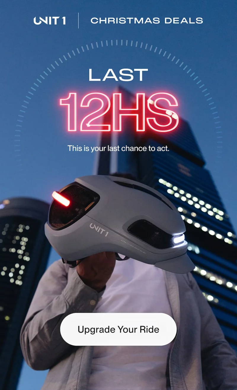 UNIT 1 smart bike helmet held at night with front white light and rear red light on, highlighting last hours of Christmas deals in a city setting