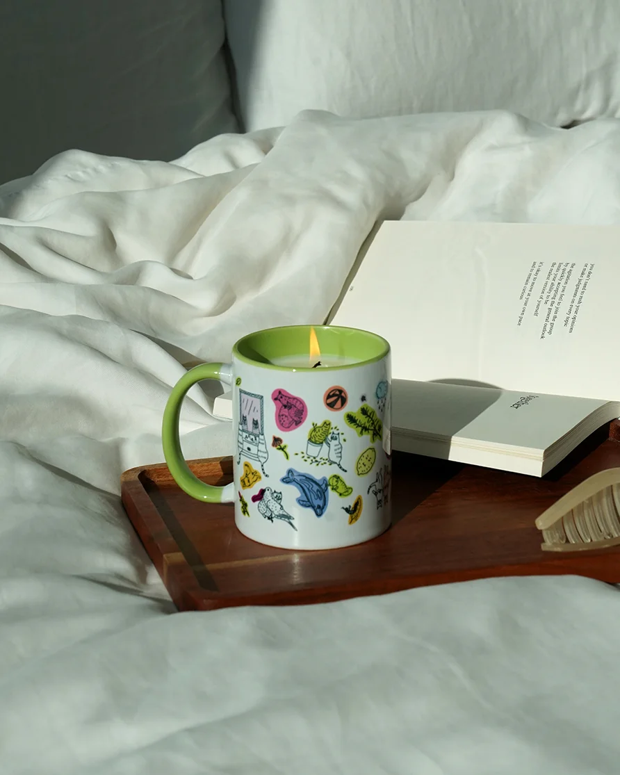 A mug candle on a book on a bed