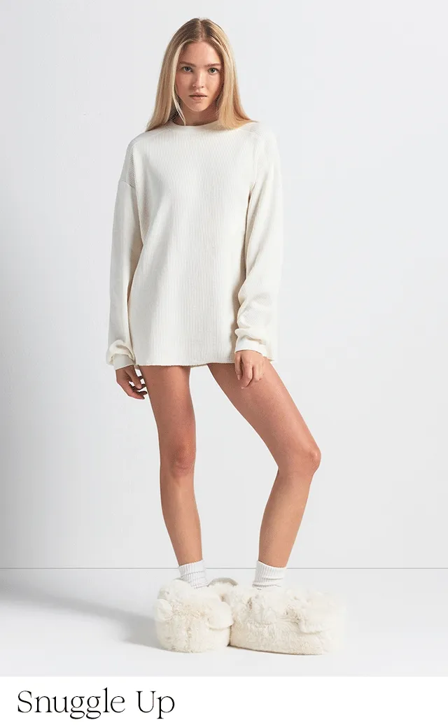 A woman wearing white teddy bear slippers and an oversized white shirt.