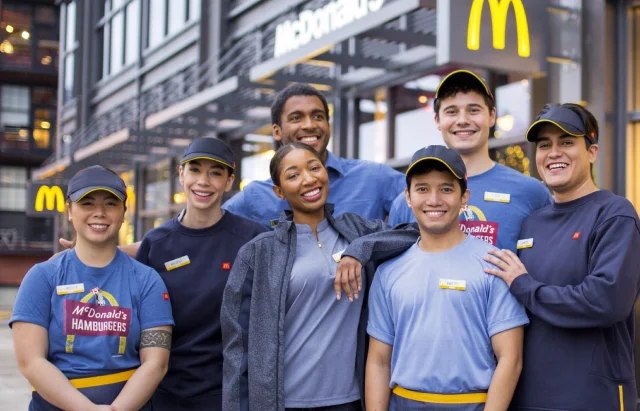 The McDonald's Crew stands in front of McDonald's. They're a diverse, supportive group, focused on making your day.