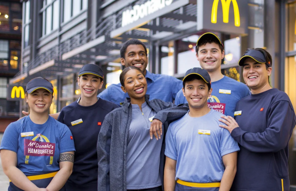 The McDonald's Crew stands in front of McDonald's. They're a diverse, supportive group, focused on making your day.