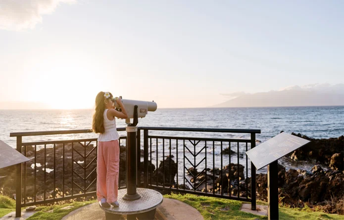 A kid looks through a telescope at the ocean in Maui.