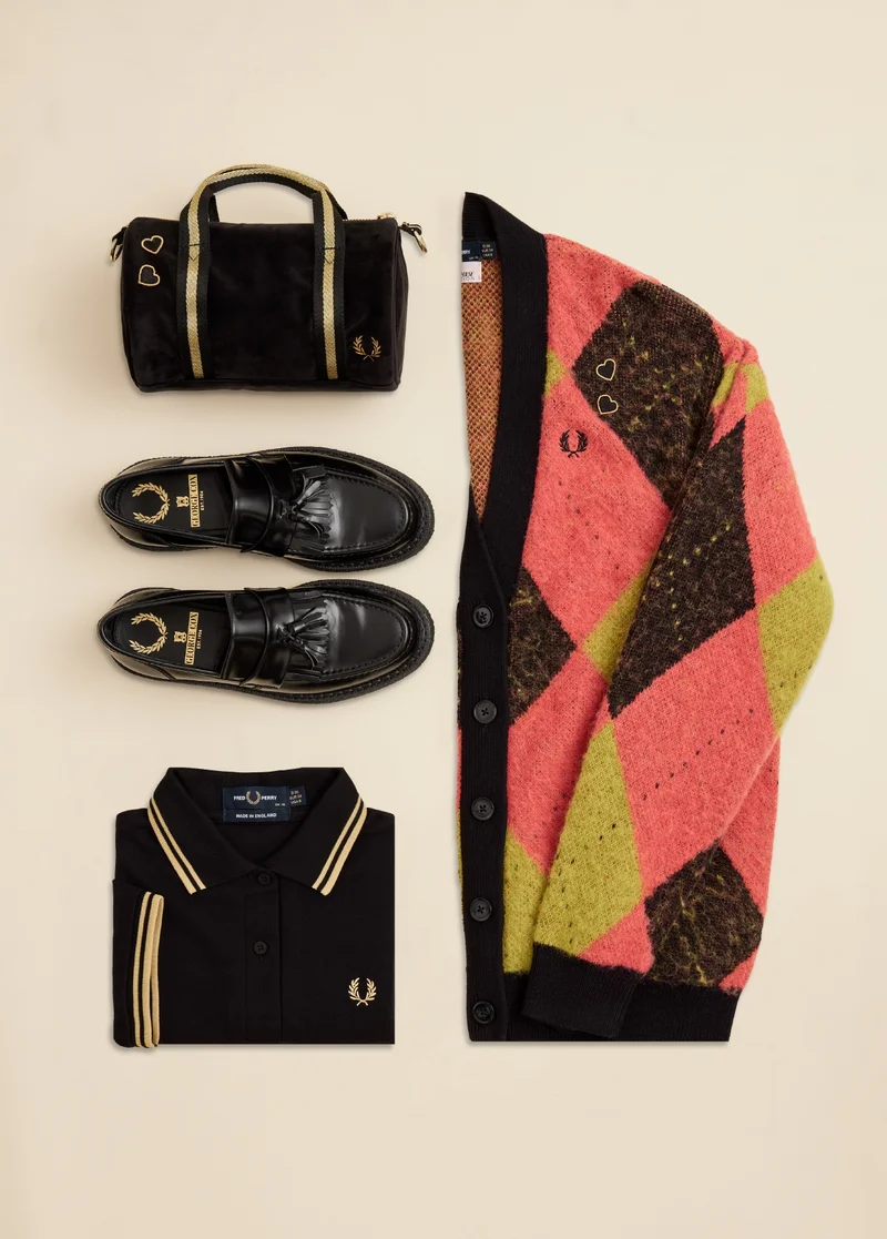 The Gift List: For Her. Image shows a folded pink, black and yellow argyle cardigan, George Cox loafers, a black and champagne tipped Fred Perry polo and a cute velvet barrel bag.
