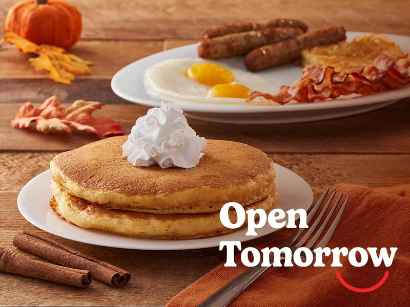 A Pumpkin Spice Pancake Combo is on a wooden table adorned with fall elements like a pumpkin and red and yellow leaves.