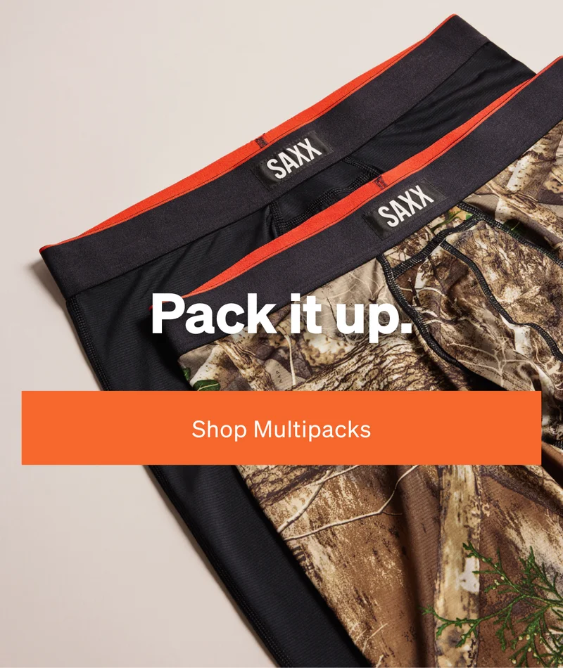 Two SAXX underwear pairs laid flat, one solid black and one camouflage print, with bold text reading “Pack it up.”