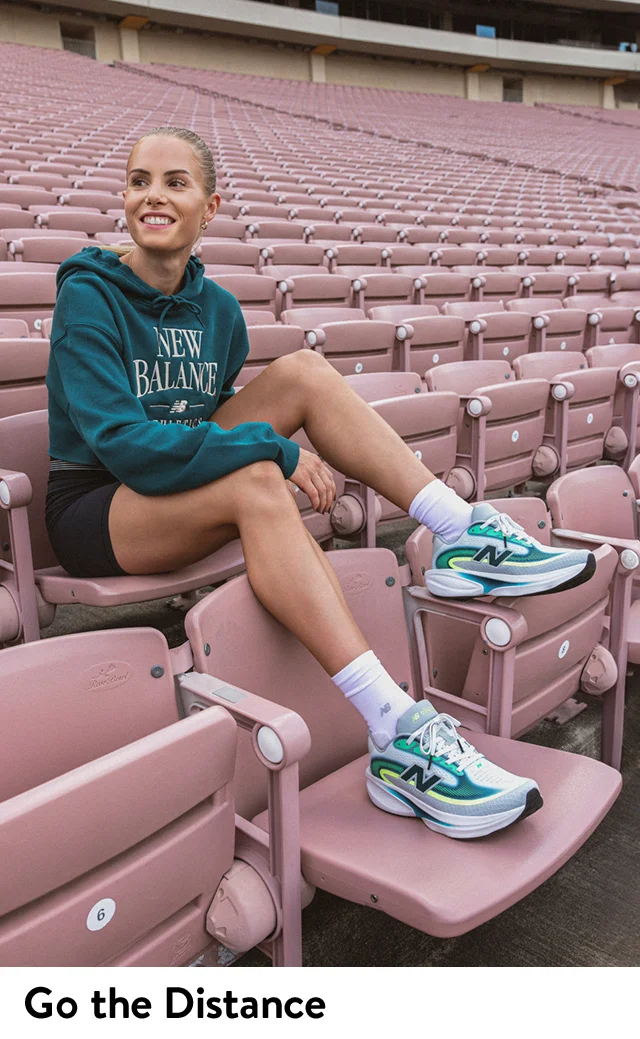 A woman sitting in a stadium wearing running clothes and New Balance sneakers.