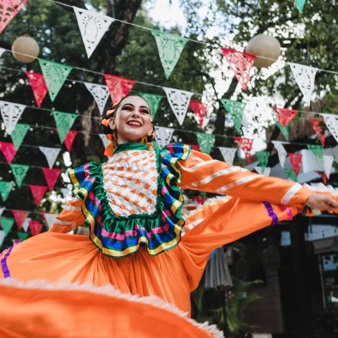 Image Description: A Mexican folklórico performer dancing in a vibrant orange Jalisco dress