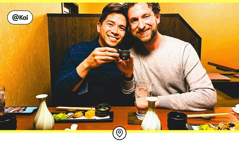 Image description: Two travelers smiling while toasting with sake cups.