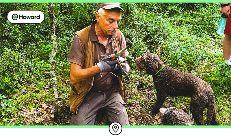 Image description: A man kneeling on the ground with a truffle hoe and a black dog.