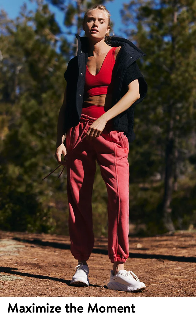 A woman wearing a red sports bra, red joggers and black vest.