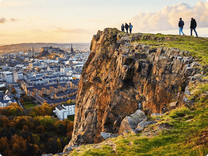 Image Description: A group of travelers admiring the Edinburgh cityscape from a hilltop in Holyrood Park