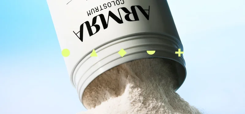 ARMRA colostrum powder pouring from an open container against a light blue background.