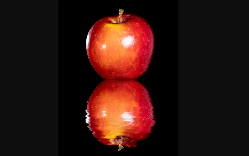 A red apple sits above its rippling reflection on a black background.