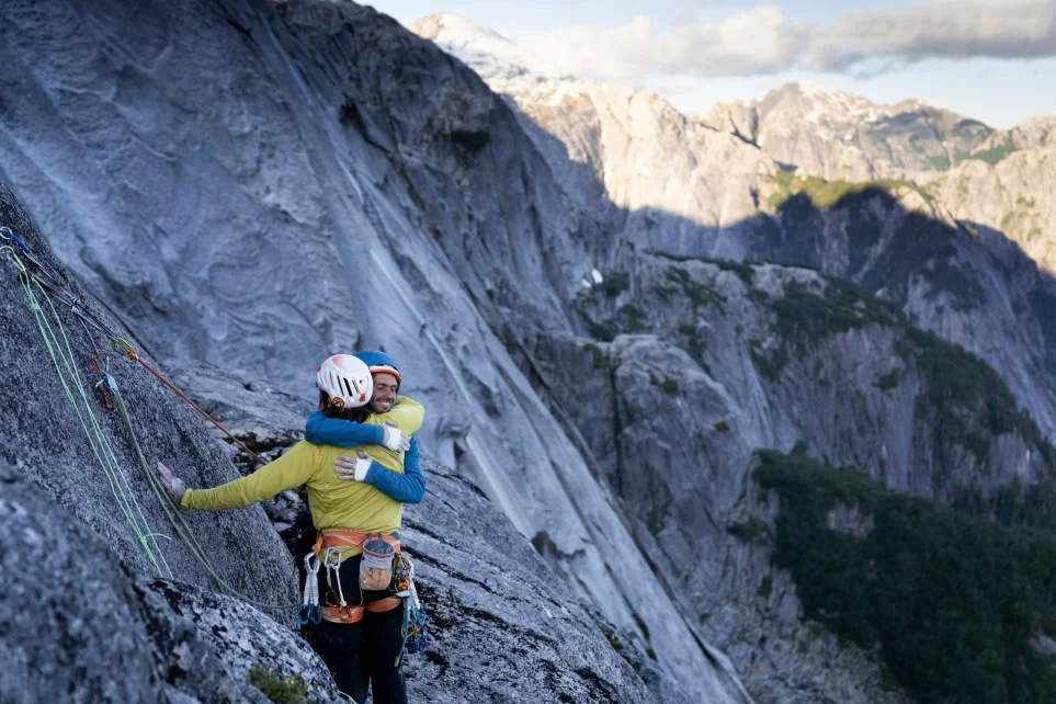 Two climbers hug at the top of their route.