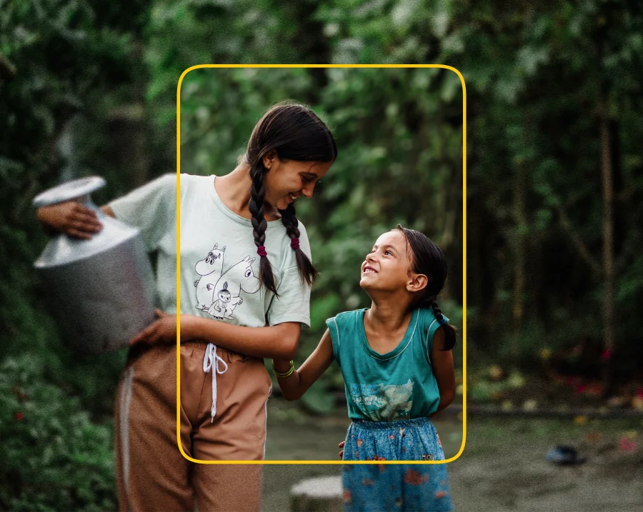 Two young girls smiling at each other while carrying a container of water.