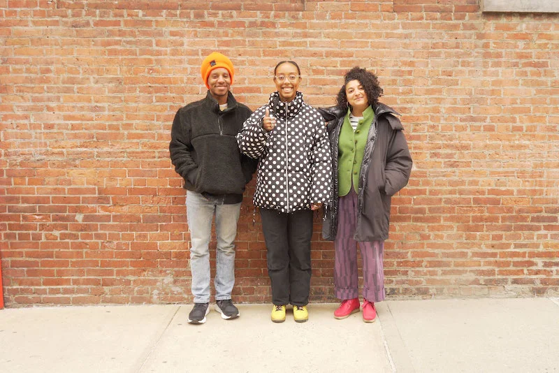 A photograph of three people standing in front of a brick wall