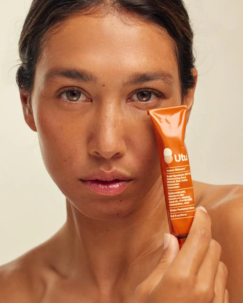 A photo of a person with tan skin holding a red tube up to their cheek.