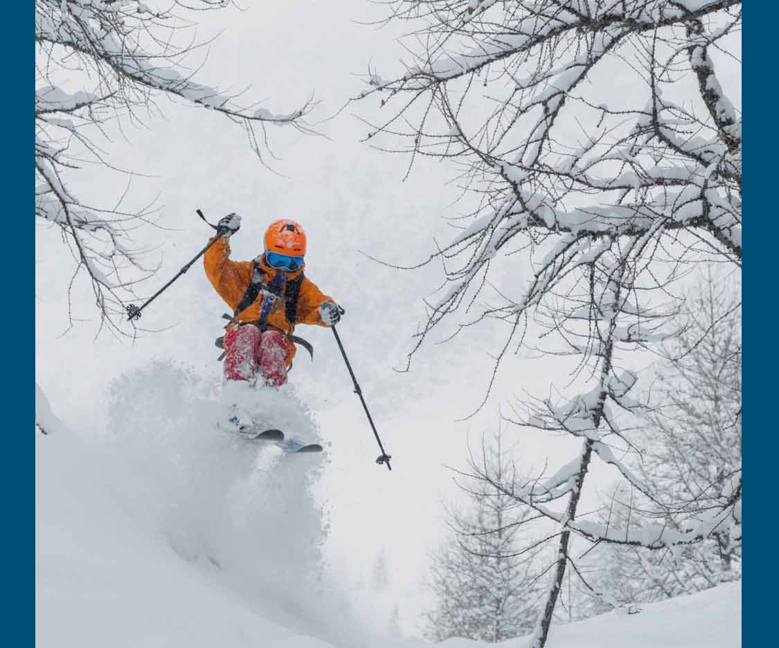 A kid hits a snowy jump on skis.