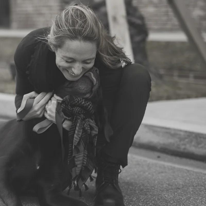 an image of a woman kneeling down petting a black dog