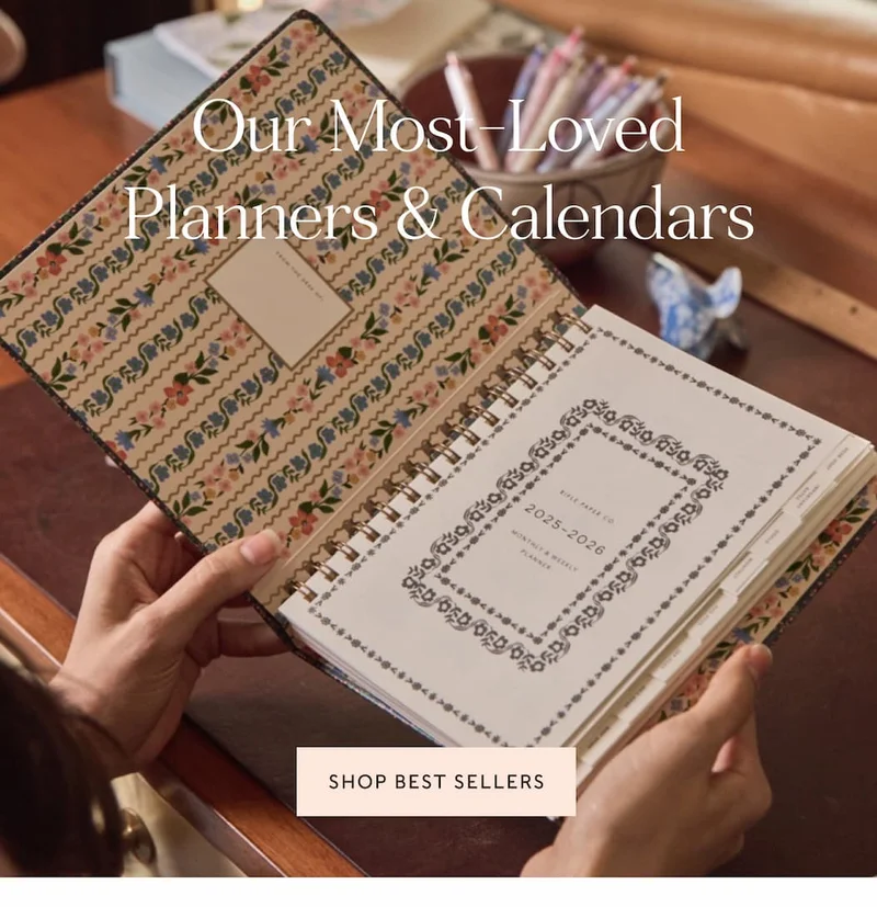 Hands holding a floral 2025-2026 planner with the text "Our Most-Loved Planners & Calendars" and a "Shop Best Sellers" button.