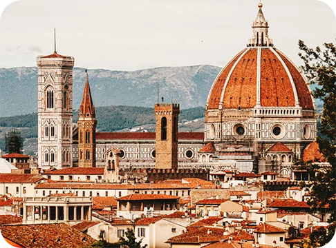 Image Description: A city skyline of ancient white buildings with red tile roofs and mountains in the background.