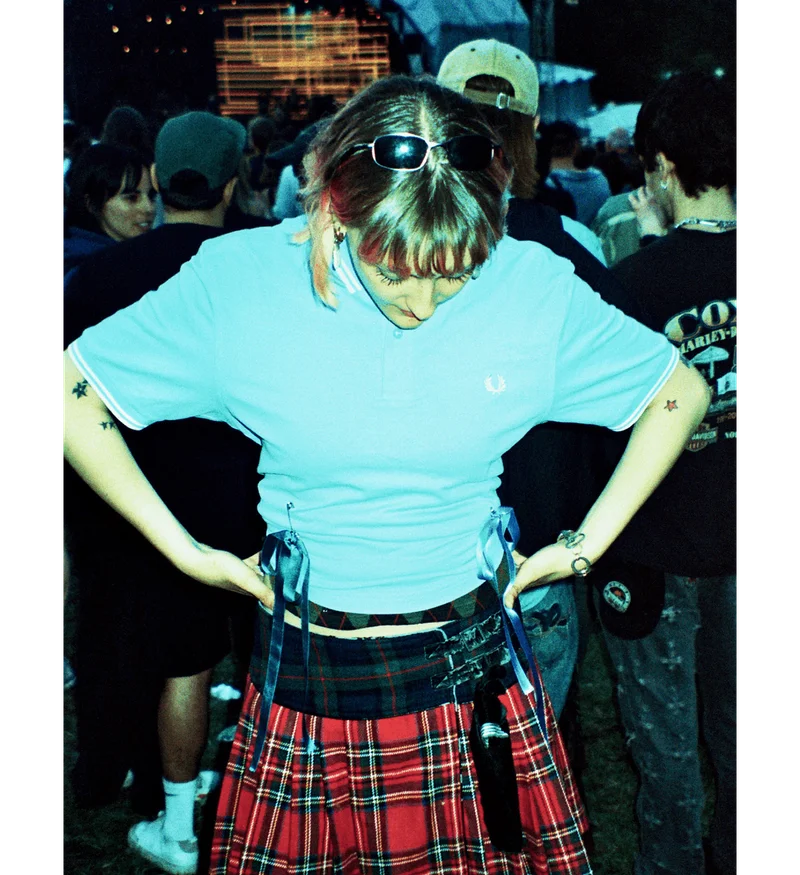 Woman at festival in a crowd wearing a blue Fred Perry Shirt that she has customised with safety pins and ribbons