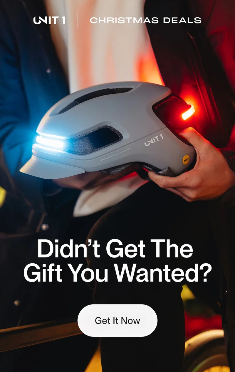 UNIT 1 smart bike helmet held in hands, showing integrated white front light and red rear light during Christmas deals promotion
