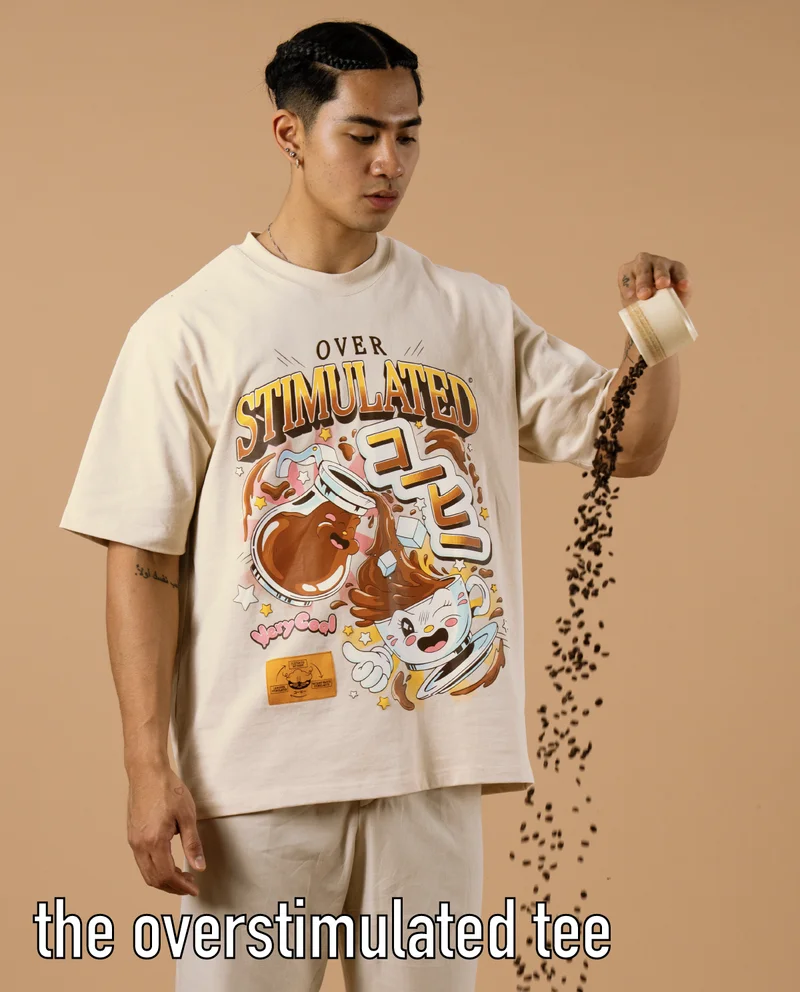 The Overstimulated Tee (man pouring coffee beans out of a mug against a tan background, wearing a graphic tee - The Overstimulated Tee)