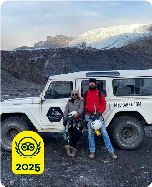 Image Description: Two people standing near a jeep with snowy mountains in the background.
