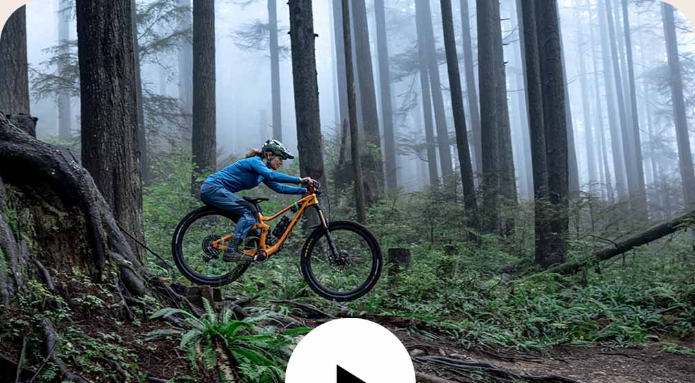 A mountain biker shifts her weight back over the seat as she descends through a foggy forest.