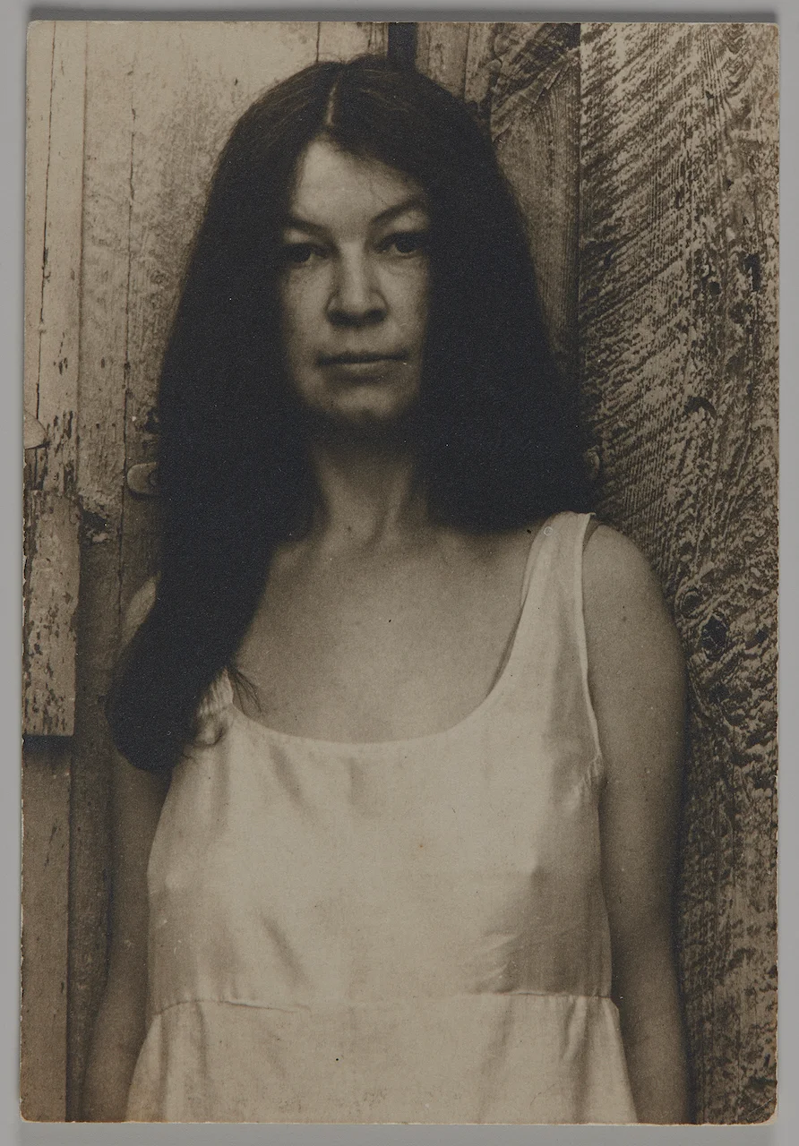 A woman in a white dress stares directly at the viewer