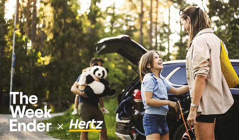 Image description: A family including two young girls and a large panda bear stuffed animal pack an electric SUV in a woodsy setting. The WeekEnder x Hertz
