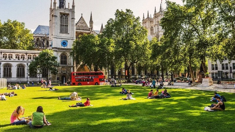 Image description: People lounge in the sun near Parliament Square and St Margaret's church in London