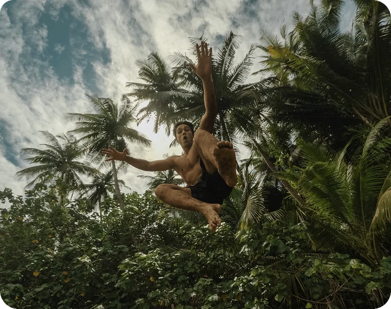 A man jumping in the air with a rainforest behind him.