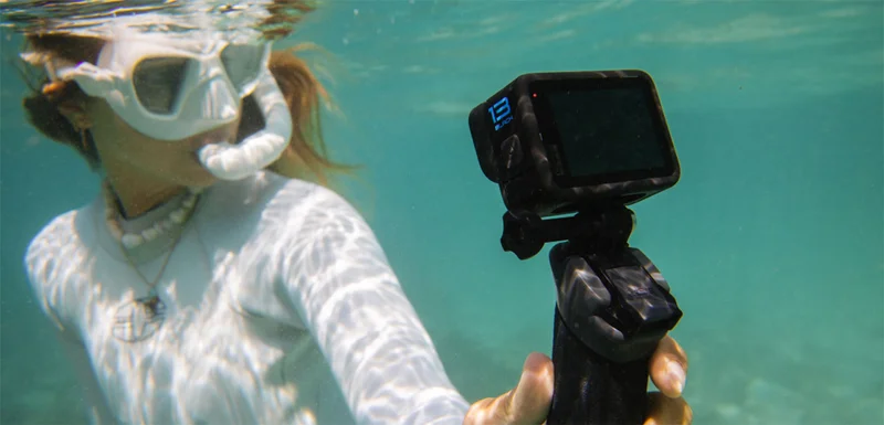A man swimming in the ocean with fish while holding a GoPro camera.