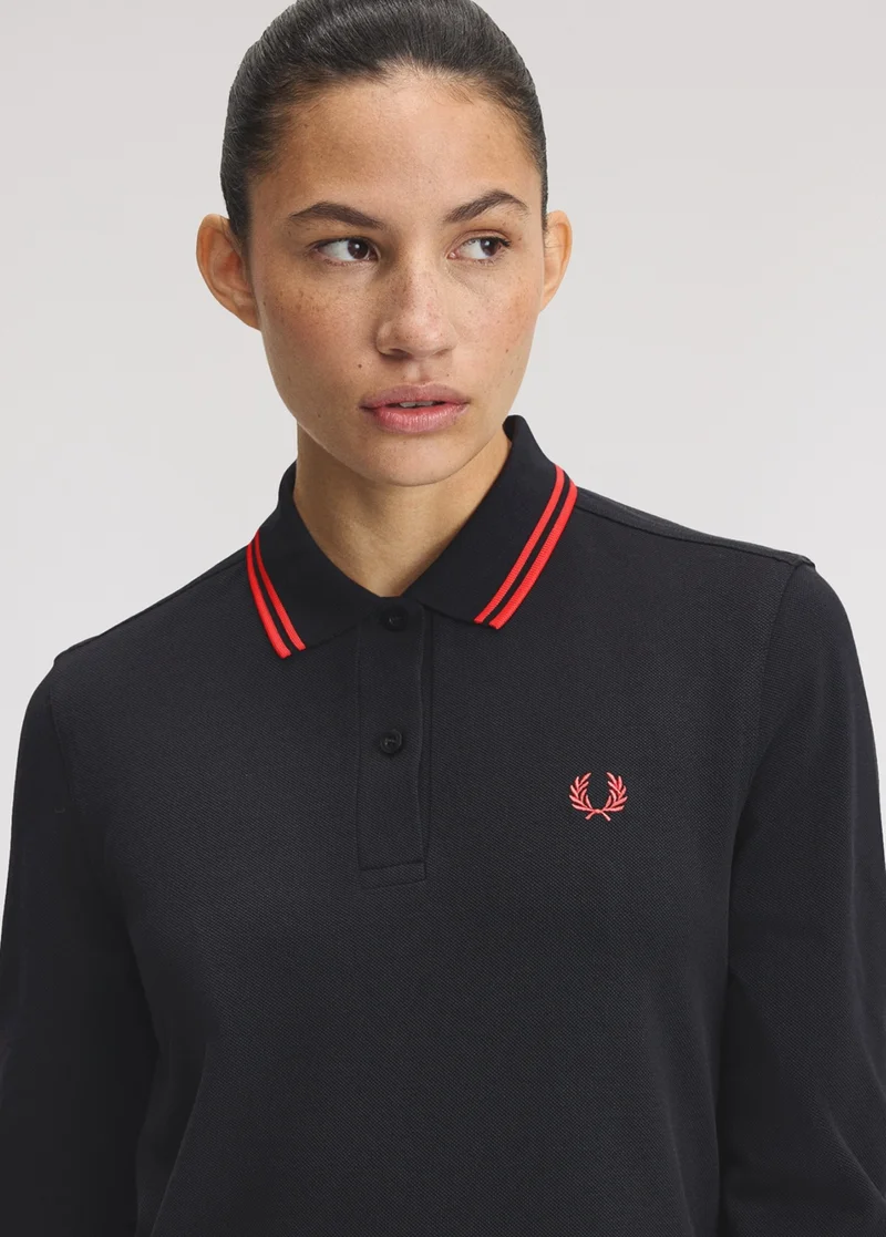 A female model wearing a twin tipped long sleeved Fred Perry Shirt in Black / Flamingo Tan / Flamingo Tan