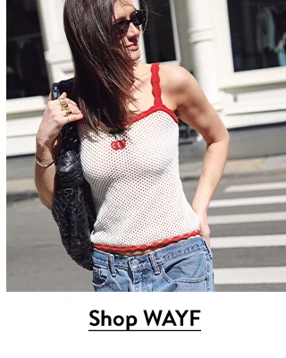A woman wearing a knit tank with a cherry embroidery and jeans.