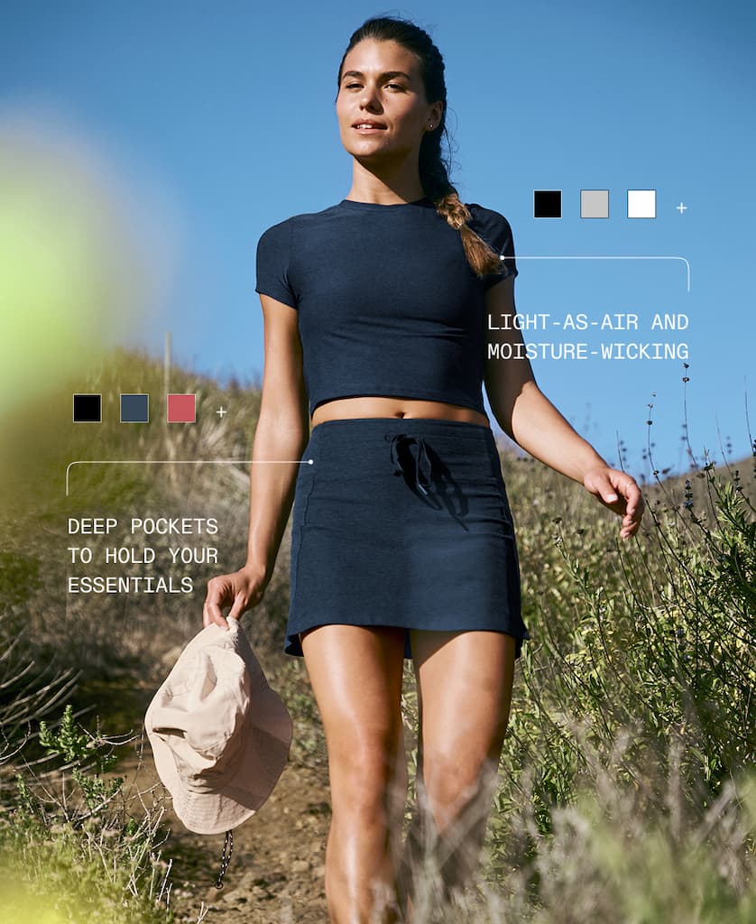 Model wearing blue cropped t-shirt and blue mini athletic skirt standing on trail.