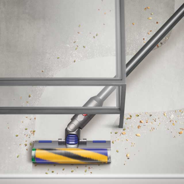 A Dyson vacuum cleaning debris under a table